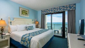 Een hotelkamer met een groot bed, een bureau, een televisie en een balkon met uitzicht op zee.