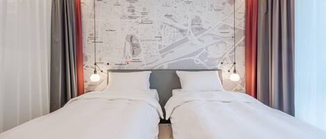 A hotel room with a large bed, two bedside tables, a map wall, and curtains.