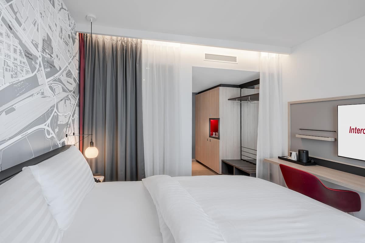 A modern hotel room with a large bed, a desk with a computer, and a TV.