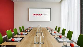 A conference room with a long table, green chairs, and a screen displaying "Intercity Hotel".
