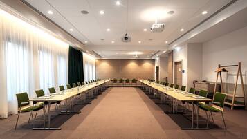 Un salón de conferencias con una larga mesa, sillas, un proyector y una ventana con cortinas.