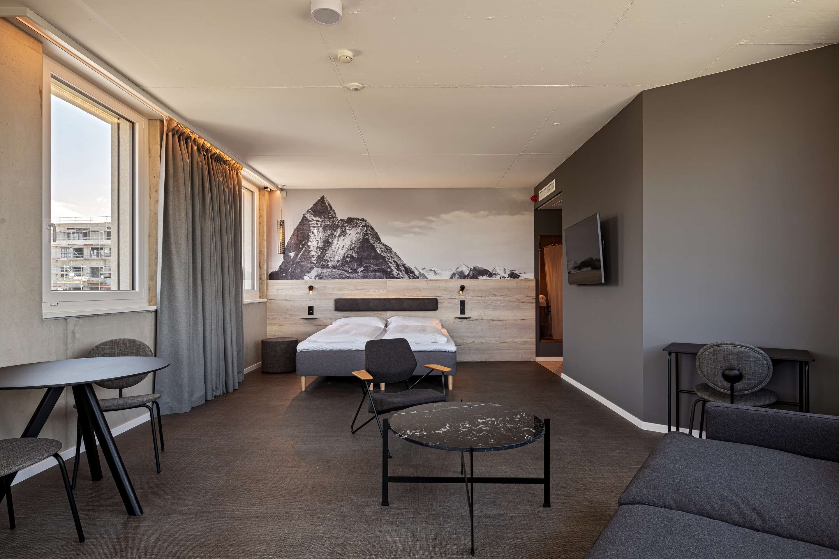 A modern hotel room with a bed, a desk, a chair, and a sofa.