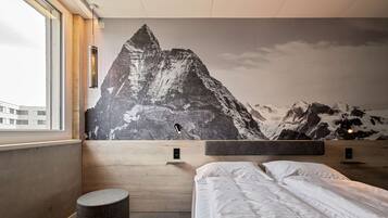 Een moderne hotelkamer met een grote bergmuur, een houten hoofdbord, een rond poefje en een net opgemaakt bed.