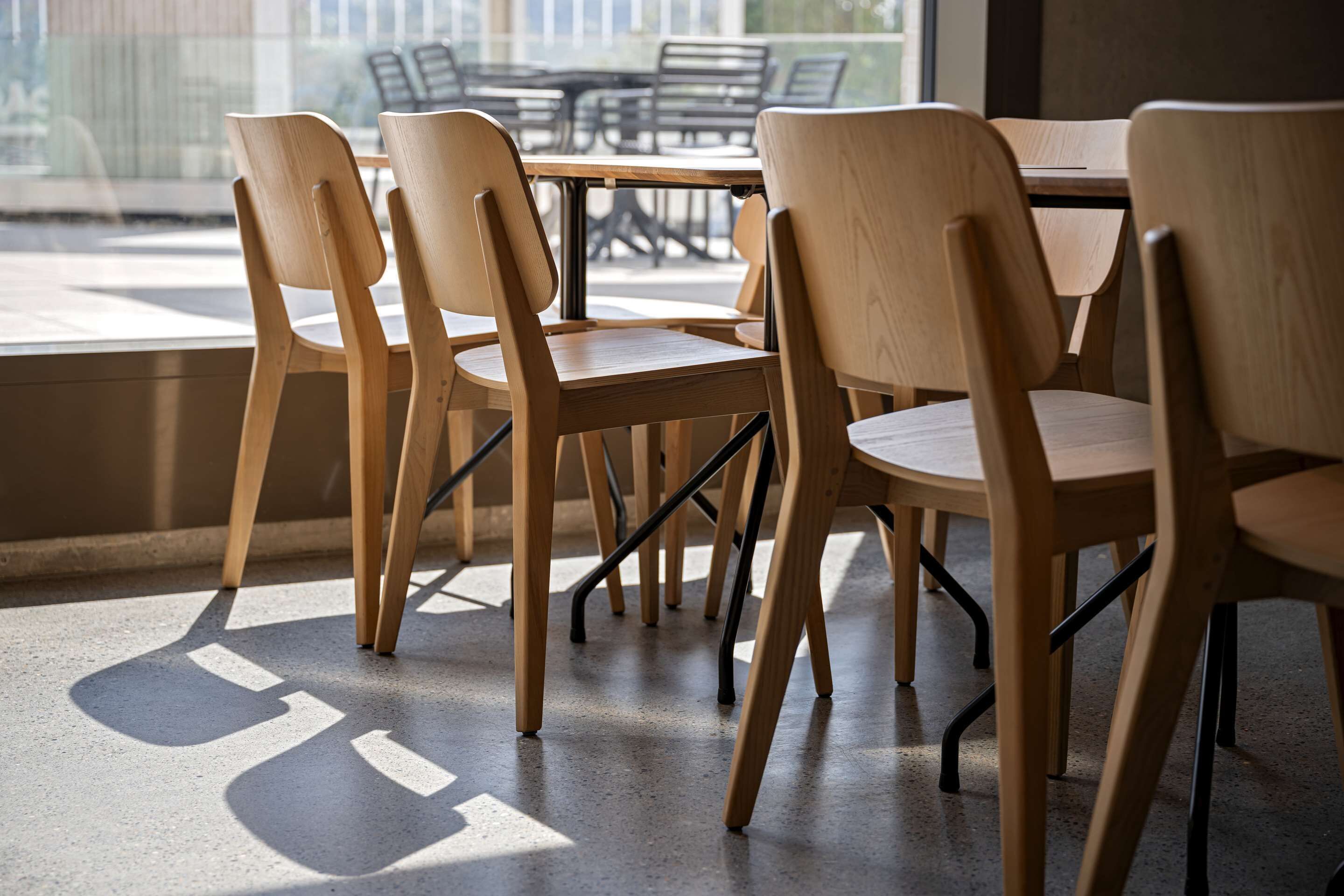 Un comedor con sillas y mesas de madera, ventanas grandes y vistas al exterior.
