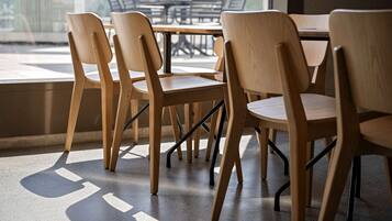 Un comedor con sillas y mesas de madera, ventanas grandes y vistas al exterior.
