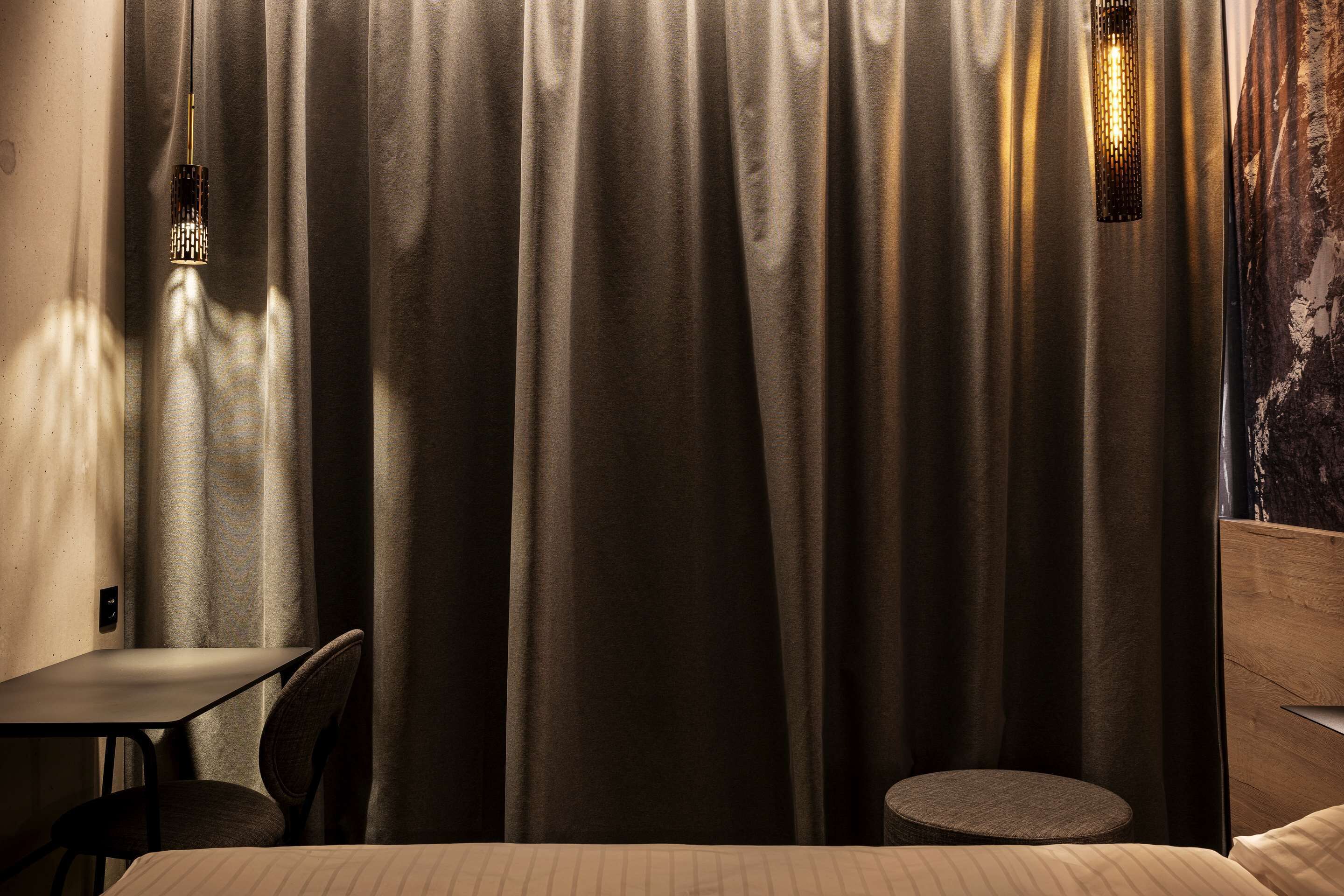 Habitación de hotel con cama, una mesita redonda, una silla y una lámpara de pared.