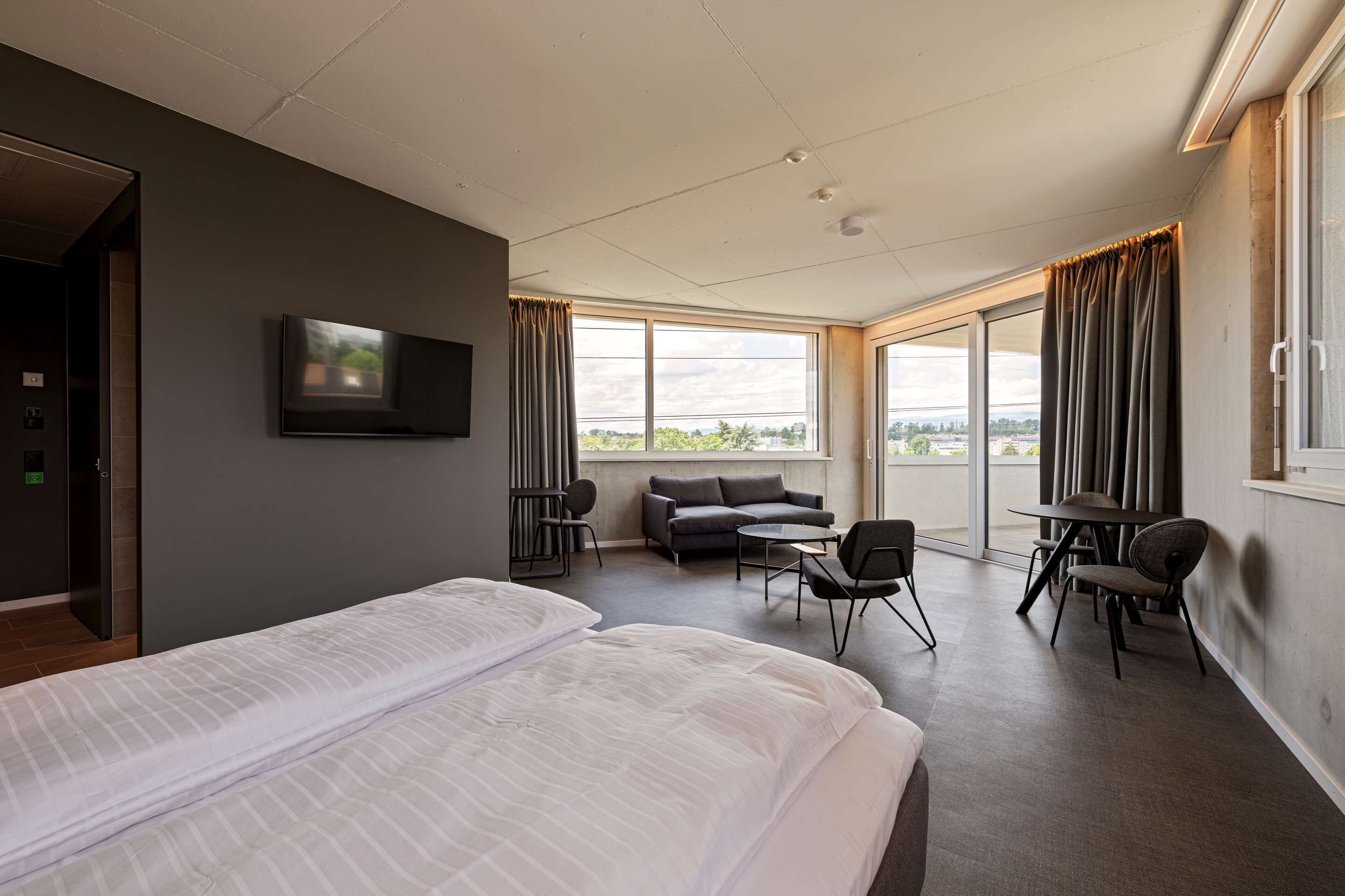 Ein modernes Hotelzimmer mit einem großen Bett, einer Couch, einem kleinen Tisch und einem an der Wand montierten Fernseher.
