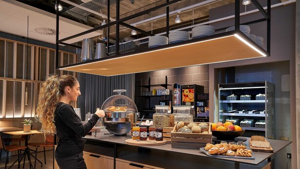 A modern kitchen with a breakfast bar, various food items, and kitchenware. - Zleep Hotel Lausanne-Chavannes (Chavannes-près-Renens)