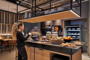 A modern kitchen with a breakfast bar, various food items, and kitchenware. - Zleep Hotel Lausanne-Chavannes (Chavannes-près-Renens)