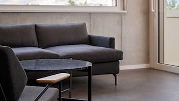 Ein modernes Wohnzimmer mit einem grauen Sofa, einem runden schwarzen Tisch und einem Holzstuhl.