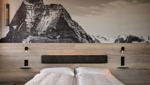 A bedroom with a wooden headboard, two bedside tables with wall-mounted lamps, and a large mountain mural on the wall. - Zleep Hotel Lausanne-Chavannes (Chavannes-près-Renens)