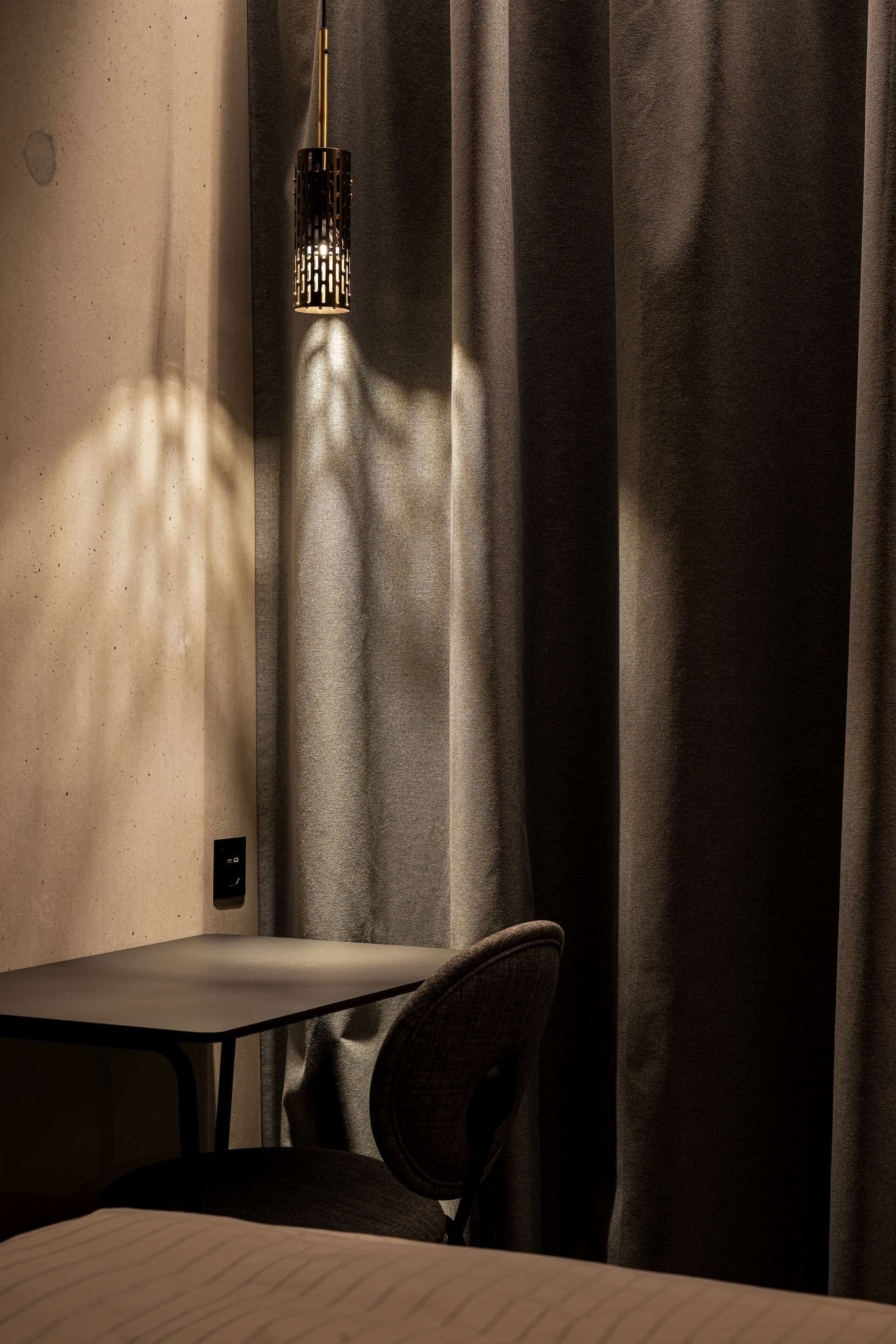 A dimly lit room with a table and a chair, a hanging light fixture, and a curtain partially drawn to the side.