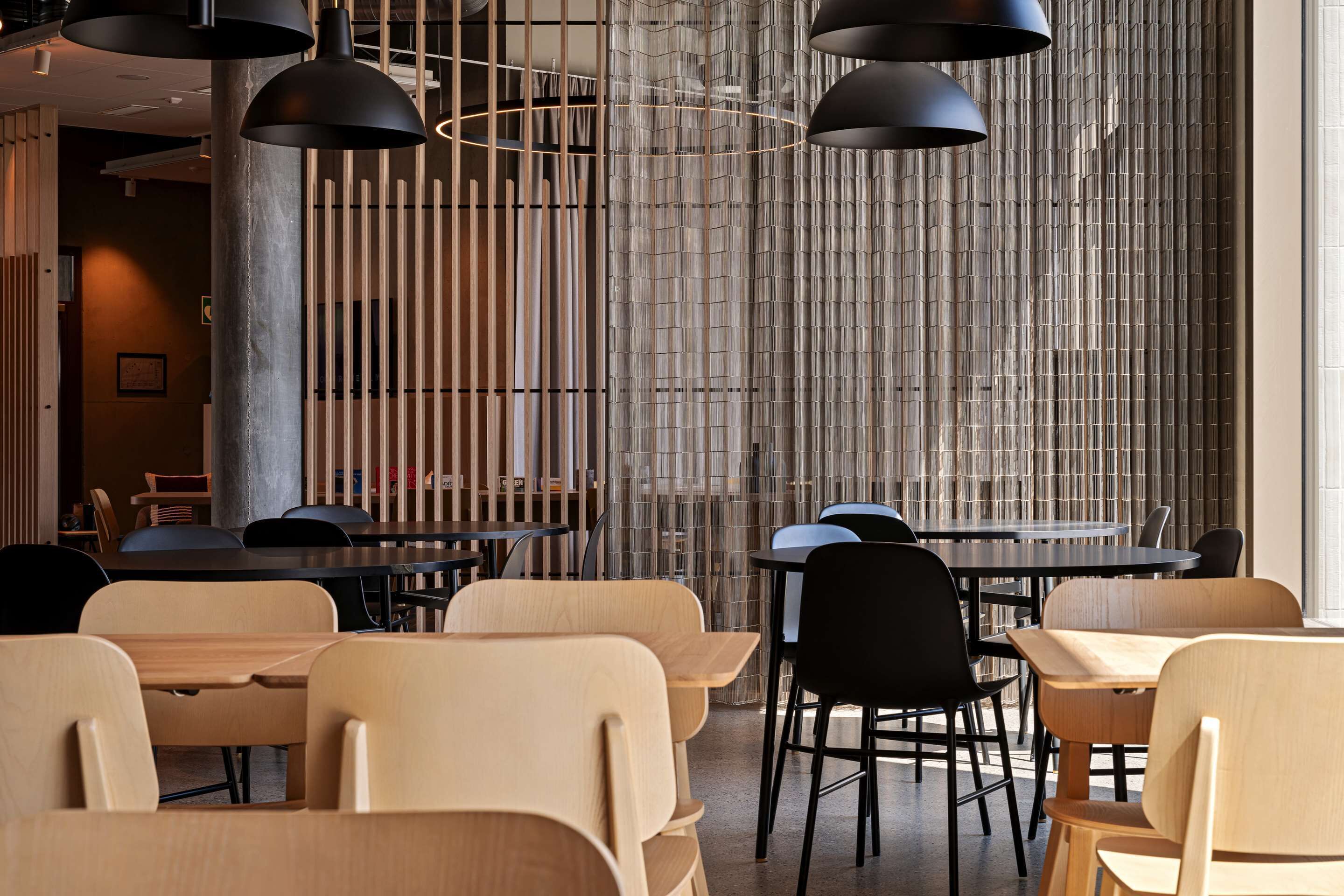 Un intérieur de restaurant moderne avec des tables et des chaises en bois, des suspensions noires et un mur en bambou.