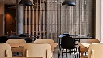Un intérieur de restaurant moderne avec des tables et des chaises en bois, des suspensions noires et un mur en bambou.
