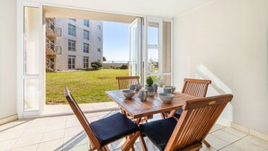 A dining area with a table and chairs, a view of a building, and a grassy yard. - Lagoon Beach 29A (Cape Town)