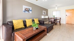A modern living room with a dark leather sofa, wooden coffee table, and a ceiling fan. - Lagoon Beach 29A (Cape Town)