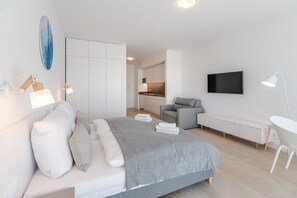 A modern bedroom with a bed, bedside lamps, a TV, and a small seating area.