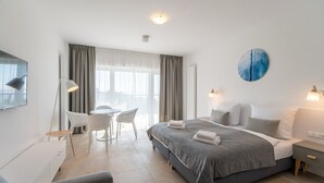 Une chambre d’hôtel moderne équipée d’un lit, de tables de chevet, d’un bureau avec des chaises et d’une grande fenêtre avec des rideaux.
