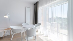 Une pièce moderne avec un coin repas comprenant des meubles blancs, un lampadaire et une grande fenêtre avec des rideaux.