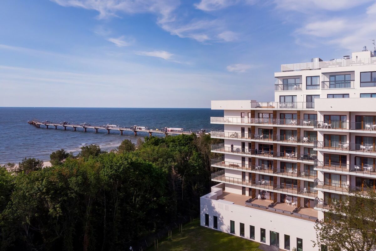 Ein mehrstöckiges Hotel mit Balkonen, die auf ein Gewässer und einen Steg blicken.