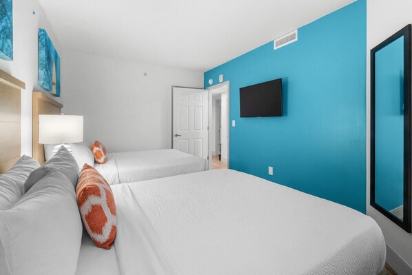Une chambre d’hôtel avec deux lits, un téléviseur fixé au mur et une porte donnant sur une autre pièce.