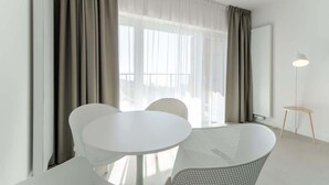 Una habitación moderna con una mesa redonda blanca, dos sillas blancas y una lámpara de pie.
