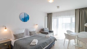 A modern hotel room with a large bed, a sitting area with a table and chairs, and a view of the city through the window.