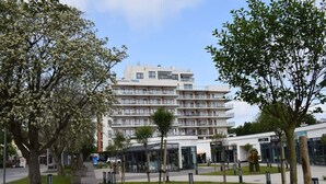 Un edificio residencial de varios pisos con balcones, un camino pavimentado y árboles.