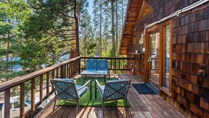 Una terraza de madera con dos sillas de diseño y una mesa, rodeada de árboles altos.