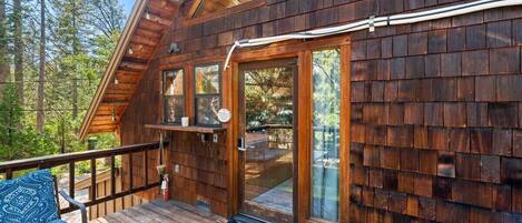 Una cabaña de madera con terraza, puerta de vidrio y una pequeña zona de estar al aire libre.