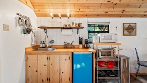 A compact kitchen with wooden cabinets, a blue refrigerator, a microwave, and a coffee machine.