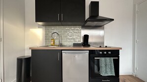 Une cuisine compacte avec des meubles noirs, une hotte de cuisine en acier inoxydable, un lave-vaisselle et un four encastré.