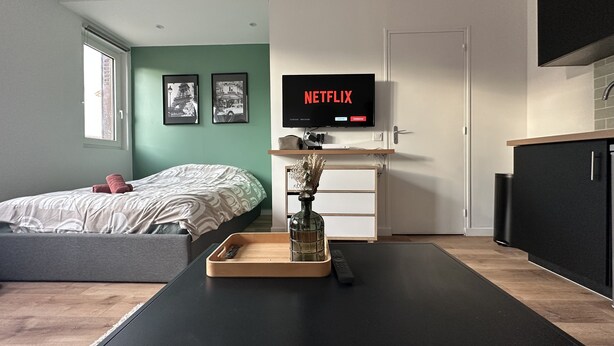 Une chambre moderne comprenant un lit, une table de chevet, un téléviseur fixé au mur et un petit coin cuisine.