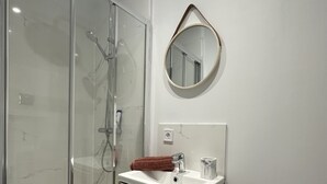 Une salle de bain avec une douche à parois de verre, un lavabo avec un miroir au-dessus et une serviette posée sur le lavabo.
