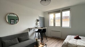 Un espace de vie compact comprenant un canapé, une petite table basse, un lit, un bureau avec une chaise et une fenêtre.