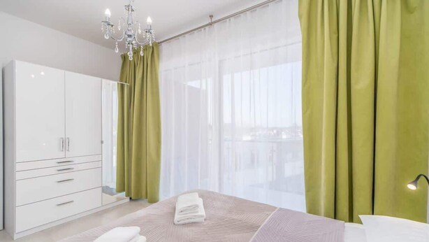 A modern bedroom with a large bed, a wardrobe, and sheer curtains.