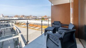 A balcony with wicker furniture, a clear view of the cityscape, and a modern building in the background.