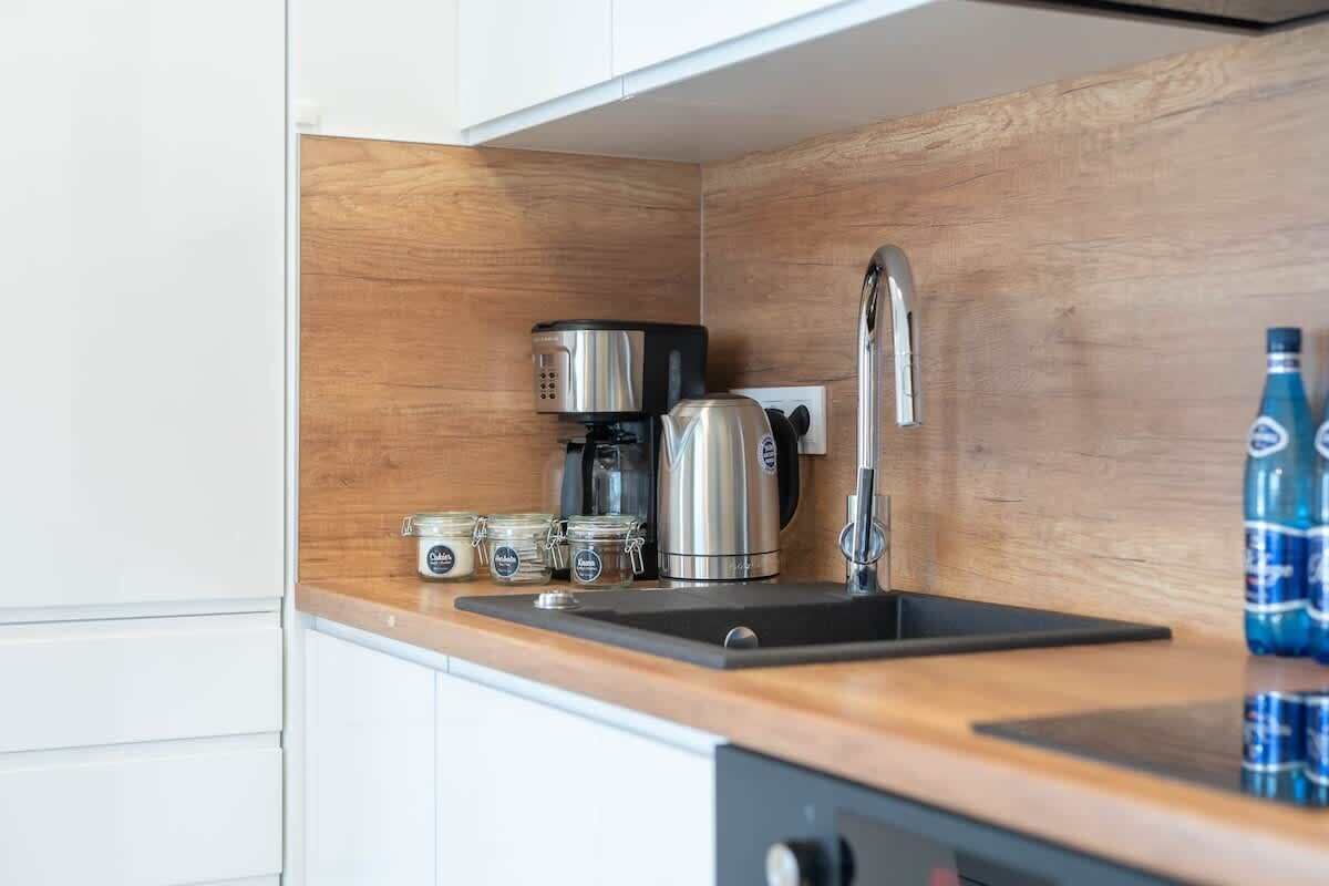 Une cuisine compacte équipée d’une machine à café en acier inoxydable, d’une bouilloire et d’un évier. Deux bouteilles d’eau sont posées sur le comptoir.