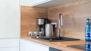 A compact kitchen with a stainless steel coffee maker, a kettle, and a sink. There are two bottles of water on the counter.