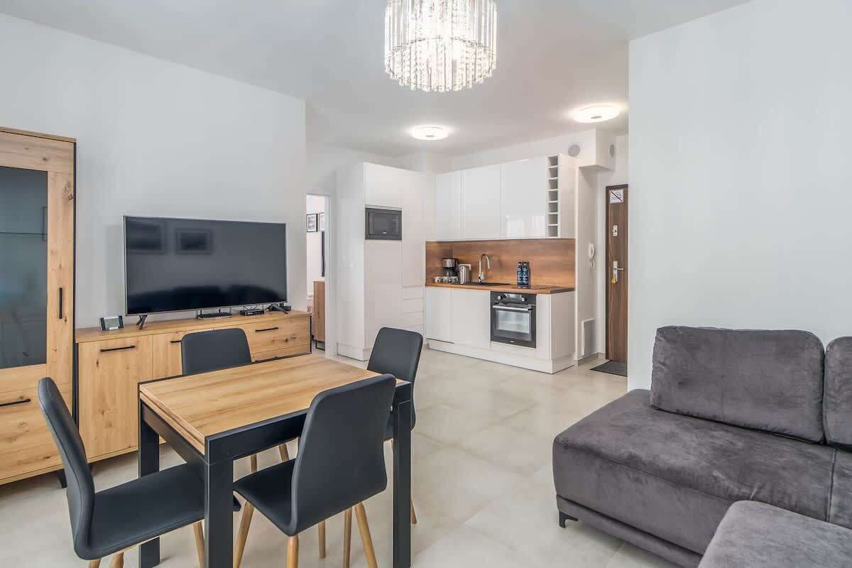 Un salon moderne avec une table à manger en bois, des chaises noires et un canapé gris.