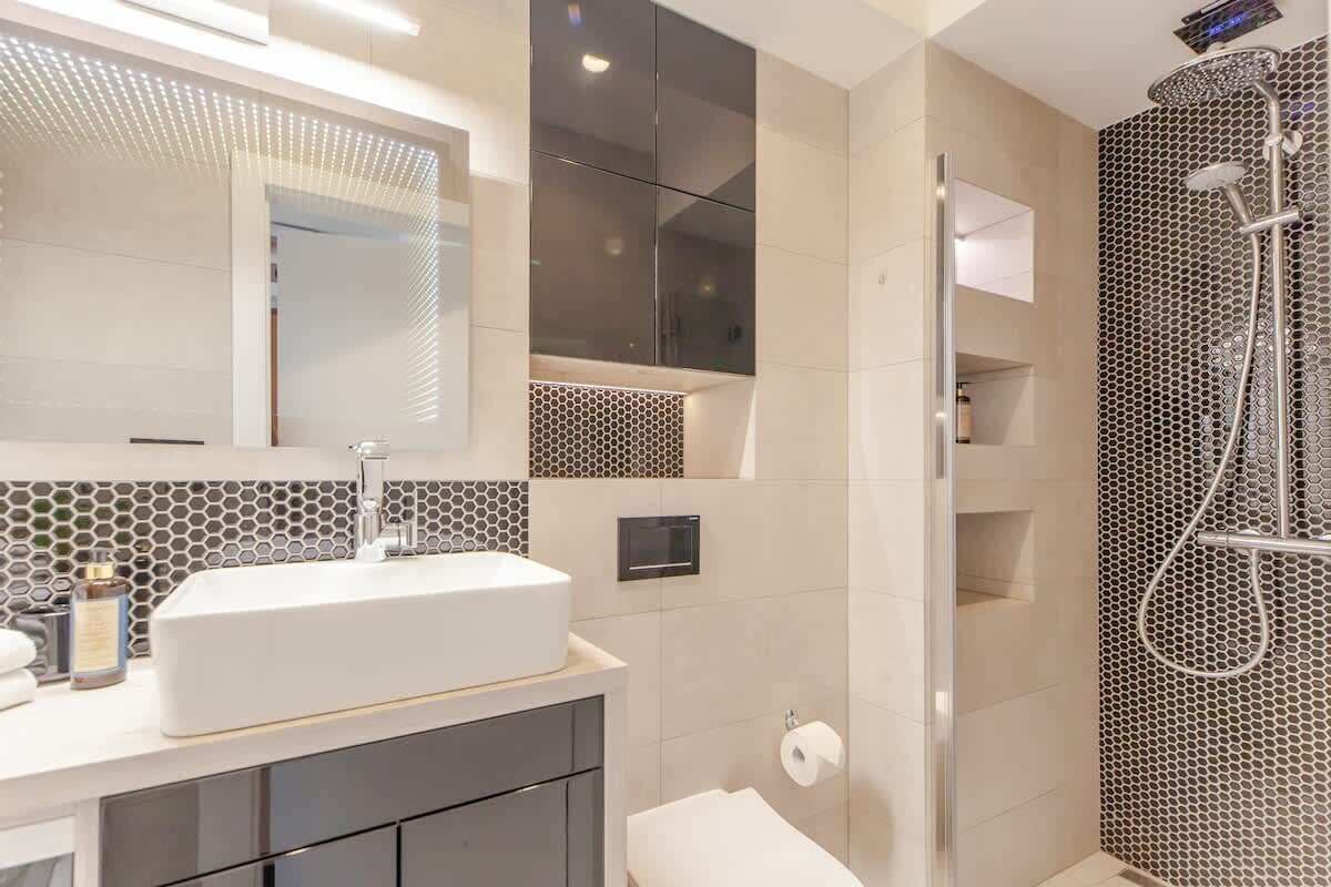 Ein modernes Badezimmer mit einem großen Spiegel, einem weißen Waschbecken und einer Dusche mit einer wabenartigen Wand.