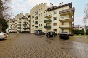 A row of multi-story residential buildings with balconies, parked cars, and a paved driveway.