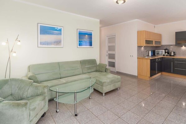 A modern living room with a sectional sofa, a glass coffee table, and a kitchen area with cabinets and appliances.
