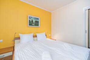 A hotel room with a bed, a nightstand, a lamp, a painting on the wall, and a door.