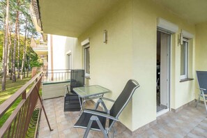 A balcony with a glass table and two chairs, a door, and a view of trees.