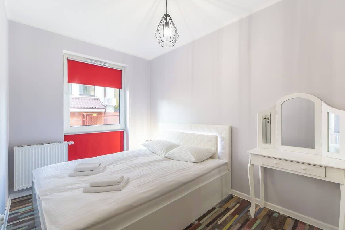 Ein Schlafzimmer mit Bett, Nachttisch, Spiegel und Fenster mit rotem Rollo.