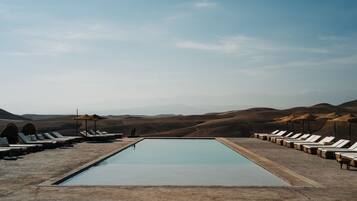 A rectangular pool with lounge chairs on both sides, set against a backdrop of rolling hills under a clear sky.