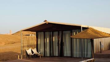A poolside area with a lounge chair, a small table, and a covered seating area with curtains.