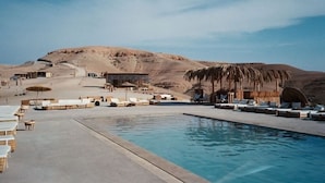 A poolside area with lounge chairs and umbrellas, set against a desert landscape with hills in the background. - Alkamar Camp Agafay (Agafay)