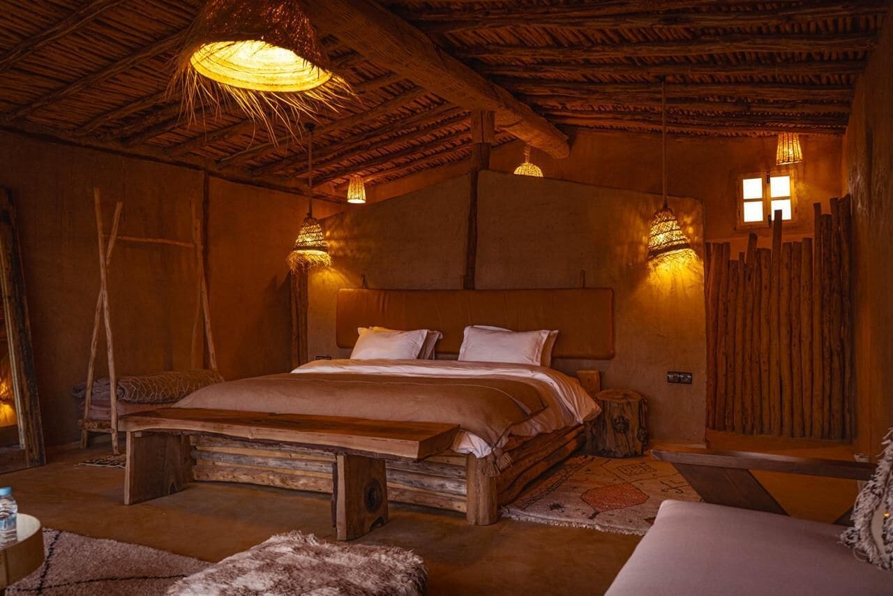 A rustic bedroom with a wooden bed, thatched ceiling, and woven light fixtures.